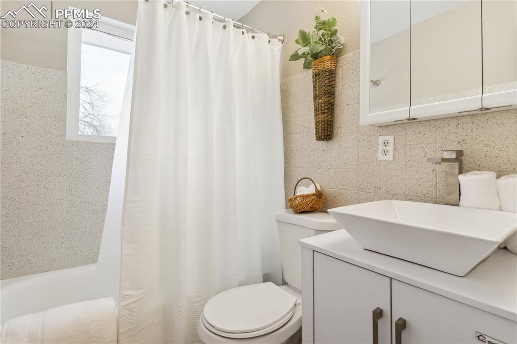 114 Chelton Road Colorado Springs, CO 80910 - Photo 10 of 18 Main floor bathroom with vanity, shower/tub combo with curtain, back splash, and tile walls