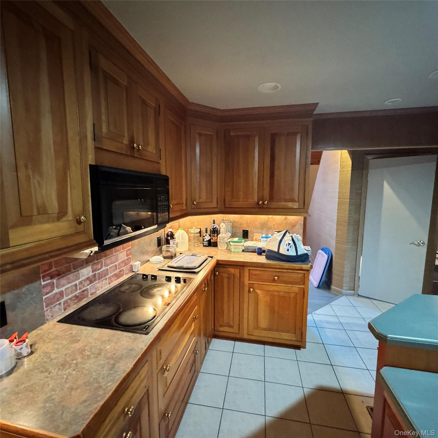 67 Steele Road New Windsor, NY 12553 - Photo 23 of 34 Wood cabinetry with under-cabinet lighting, built-in microwave, electric cooktop, brick-patterned backsplash, and tiled flooring