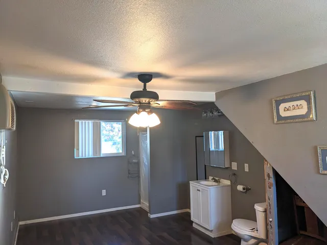 a view of an empty room with wooden floor and fan