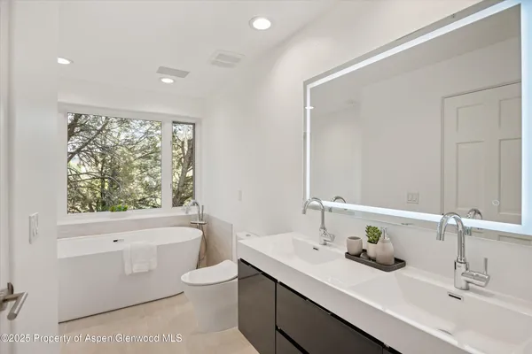 a bathroom with a toilet a sink a mirror a window and vanity