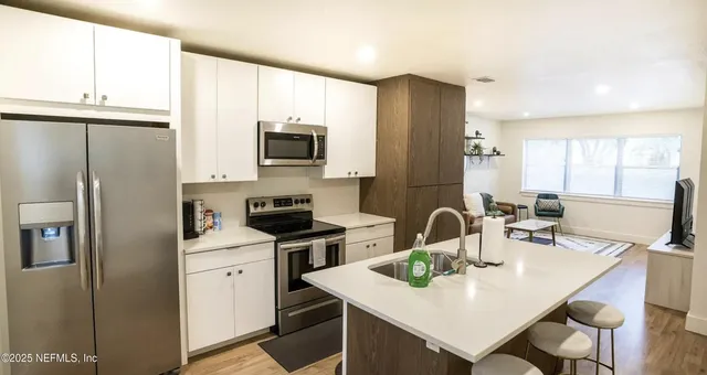 a kitchen with a refrigerator a stove a sink and white cabinets with wooden floor