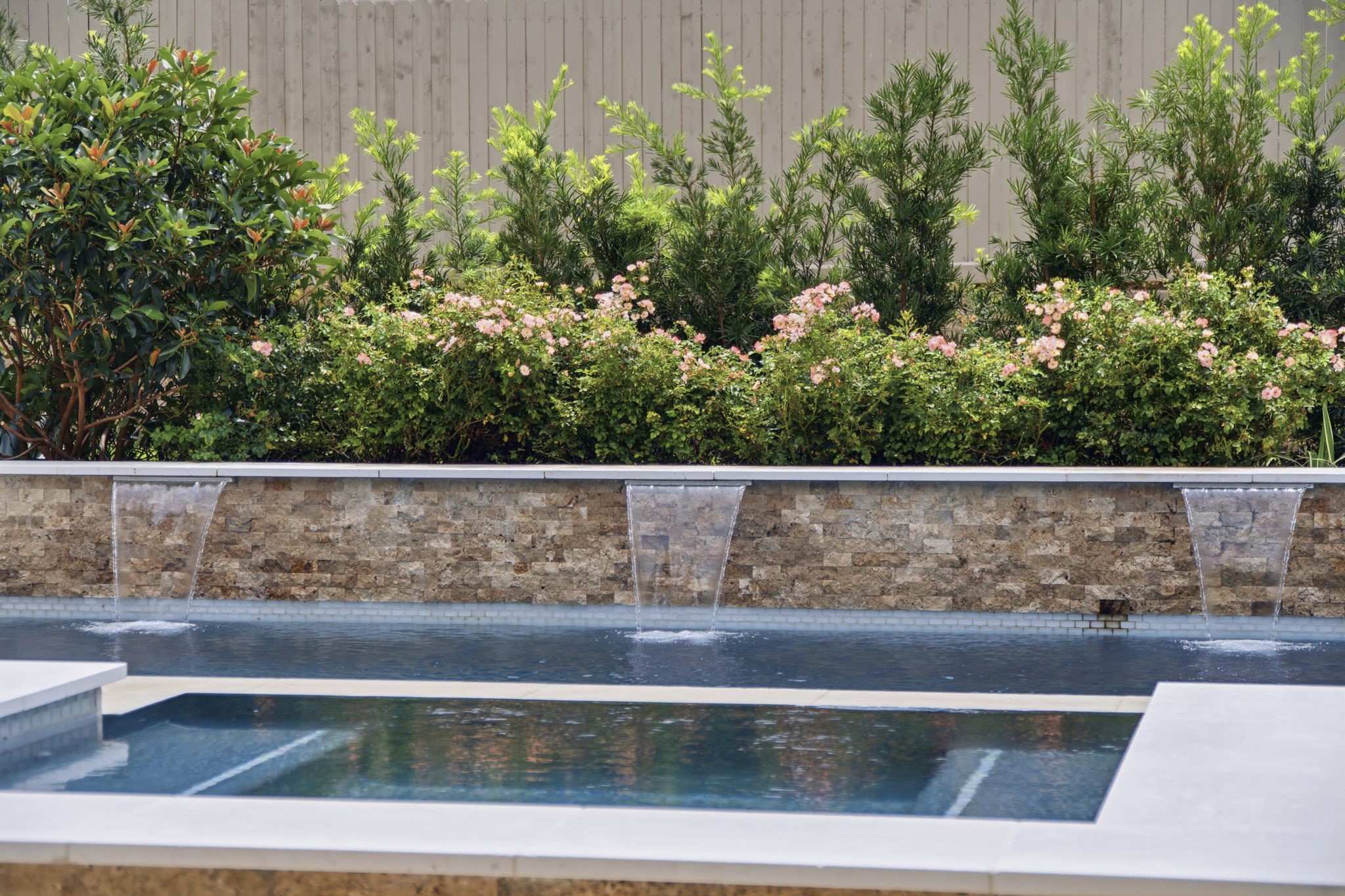 14012 Beartooth Bend Trail Conroe, TX 77384 - Photo 41 of 50 The pool is anchored by a stunning stone accent wall featuring three cascading waterfall features that provide both visual appeal and the soothing sound of flowing water. Lush tropical landscaping surrounds the space, enhancing the private, tranquil atmosphere and creating the feeling of an exclusive backyard retreat.