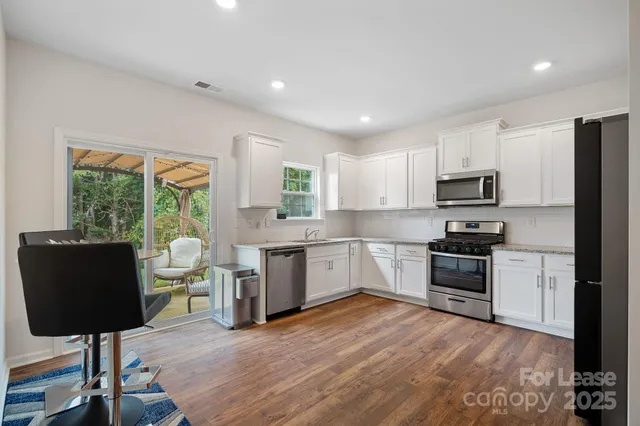 a kitchen with stainless steel appliances granite countertop a stove top oven a sink dishwasher a dining table and chairs with wooden floor