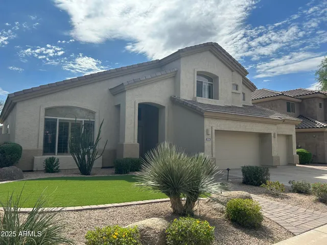 a view of a white house next to a yard with potted plants