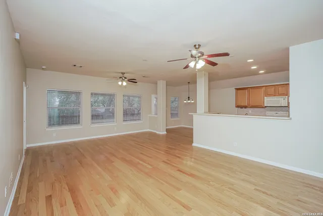a view of an empty room with wooden floor and a ceiling fan
