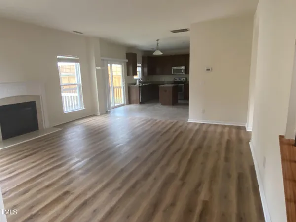 a view of empty room with wooden floor and kitchen