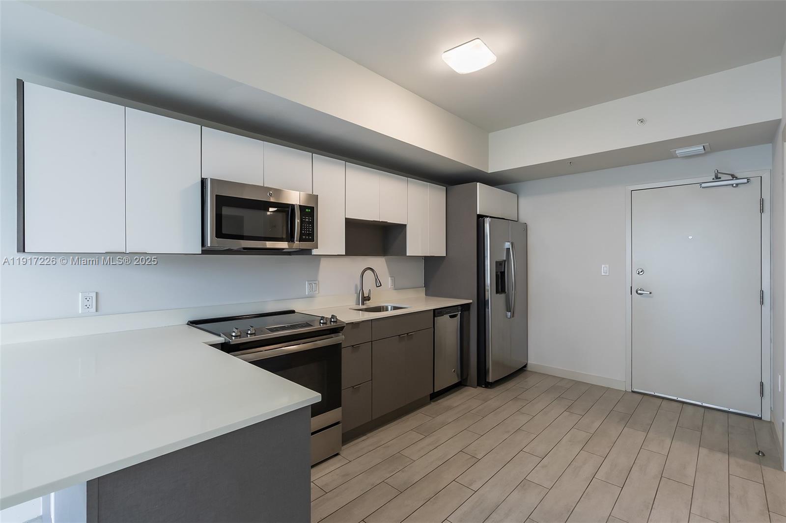 321 Northeast 26th Street, Unit 614 Miami, FL 33137 - Photo 5 of 22 a kitchen with stainless steel appliances a sink dishwasher a stove top oven a refrigerator with grey cabinets and wooden floor