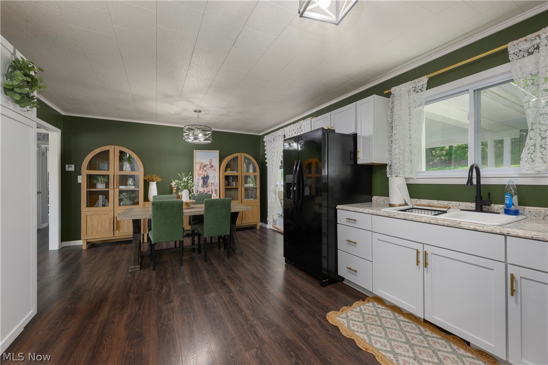 6105 Wolf Run Road Southeast Dennison, OH 44621 - Photo 22 of 35 Kitchen and dining area featuring dark wood-finish flooring, white cabinetry with gold-tone hardware, light-toned countertops, a black sink with a matte black faucet, and olive green walls