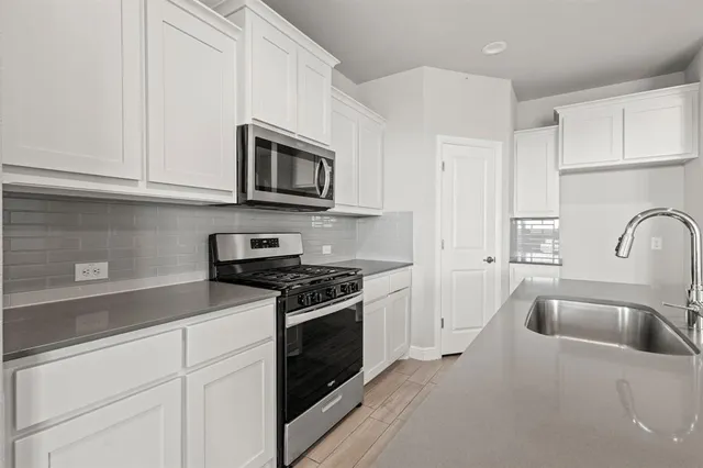 a kitchen with stainless steel appliances granite countertop white cabinets a sink a stove and a refrigerator
