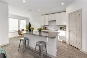 7811 Golden Rubia Lane Rosharon, TX 77583 - Photo 3 of 10 This photo showcases a modern kitchen with a central island and bar seating. It features white cabinetry, a subway tile backsplash, and stainless steel fixtures. The space is well-lit with natural light and has a cozy dining area nearby.