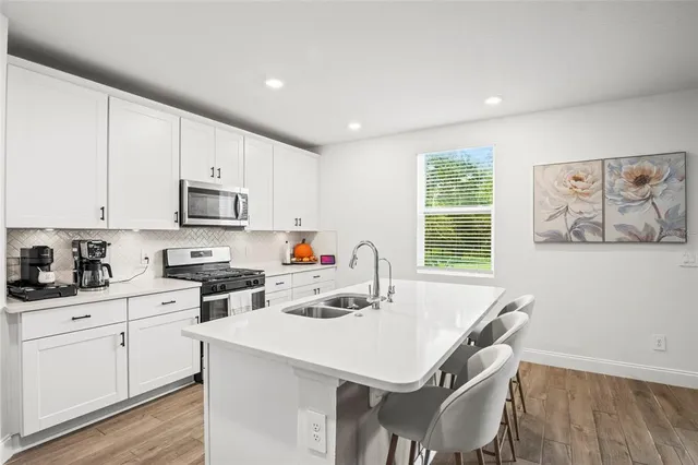 a kitchen with stainless steel appliances a stove a sink a refrigerator white cabinets and wooden floor