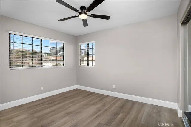 an empty room with wooden floor ceiling fan and windows