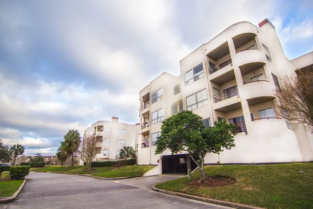 a front view of a multi story residential apartment building with yard and parking space