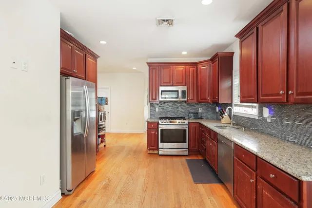 a kitchen with stainless steel appliances granite countertop a refrigerator a sink dishwasher a stove with wooden cabinets and floor