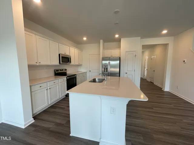 a kitchen with kitchen island granite countertop a sink a stove a refrigerator cabinets and wooden floor