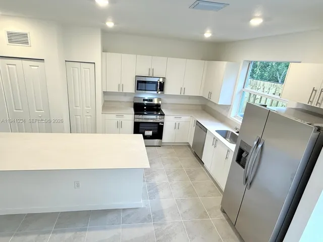 a large kitchen with stainless steel appliances a stove a refrigerator a sink a washer dryer and white cabinets