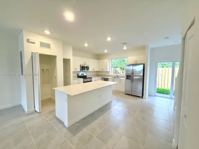 a large white kitchen with refrigerator a sink and a large window