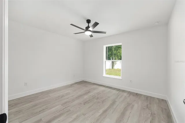 an empty room with wooden floor ceiling fan and window