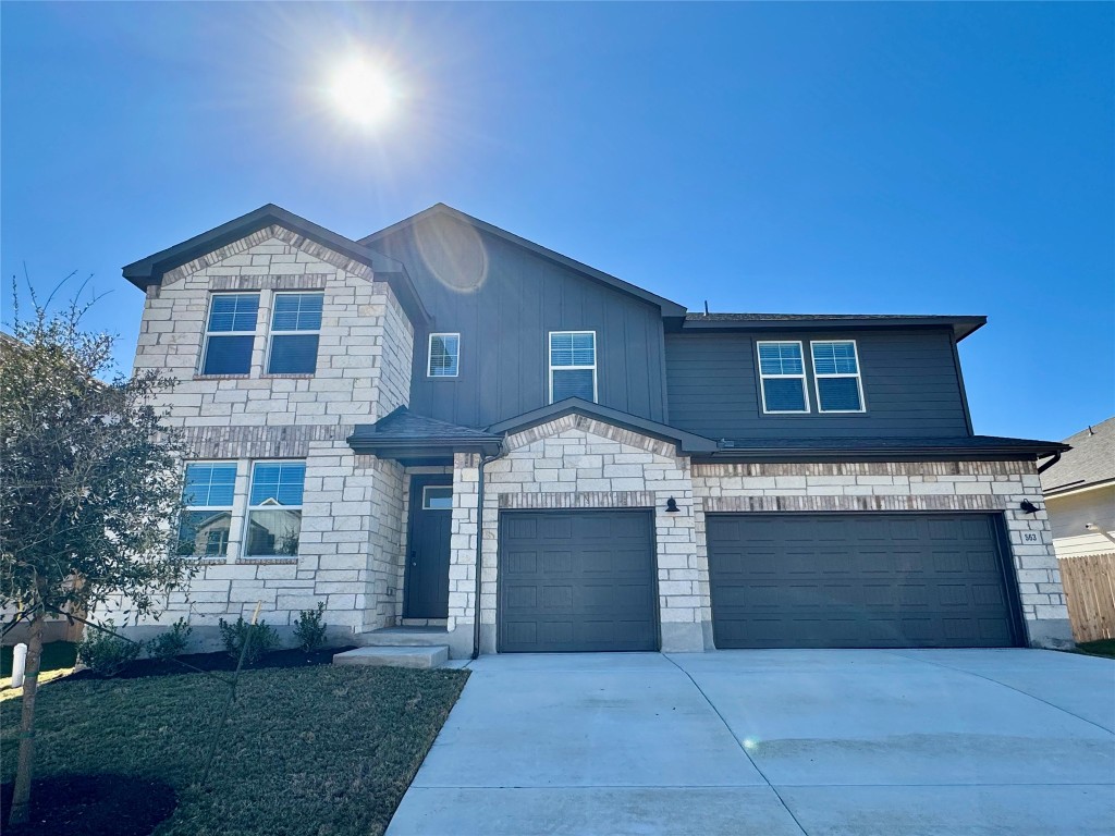 View of front of property featuring driveway, an attached garage, stone siding, and a front lawn
