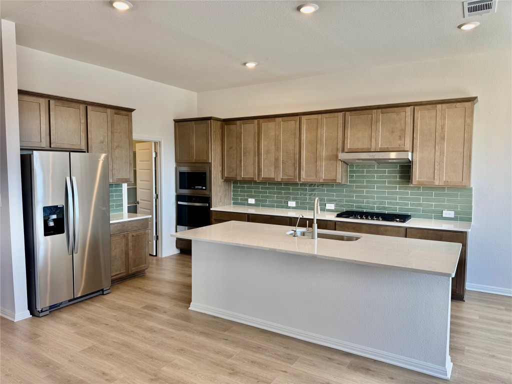 563 Banff Drive Kyle, TX 78640 - Photo 2 of 7 Kitchen featuring appliances with stainless steel finishes, tasteful backsplash, recessed lighting, light stone counters, and light wood-type flooring