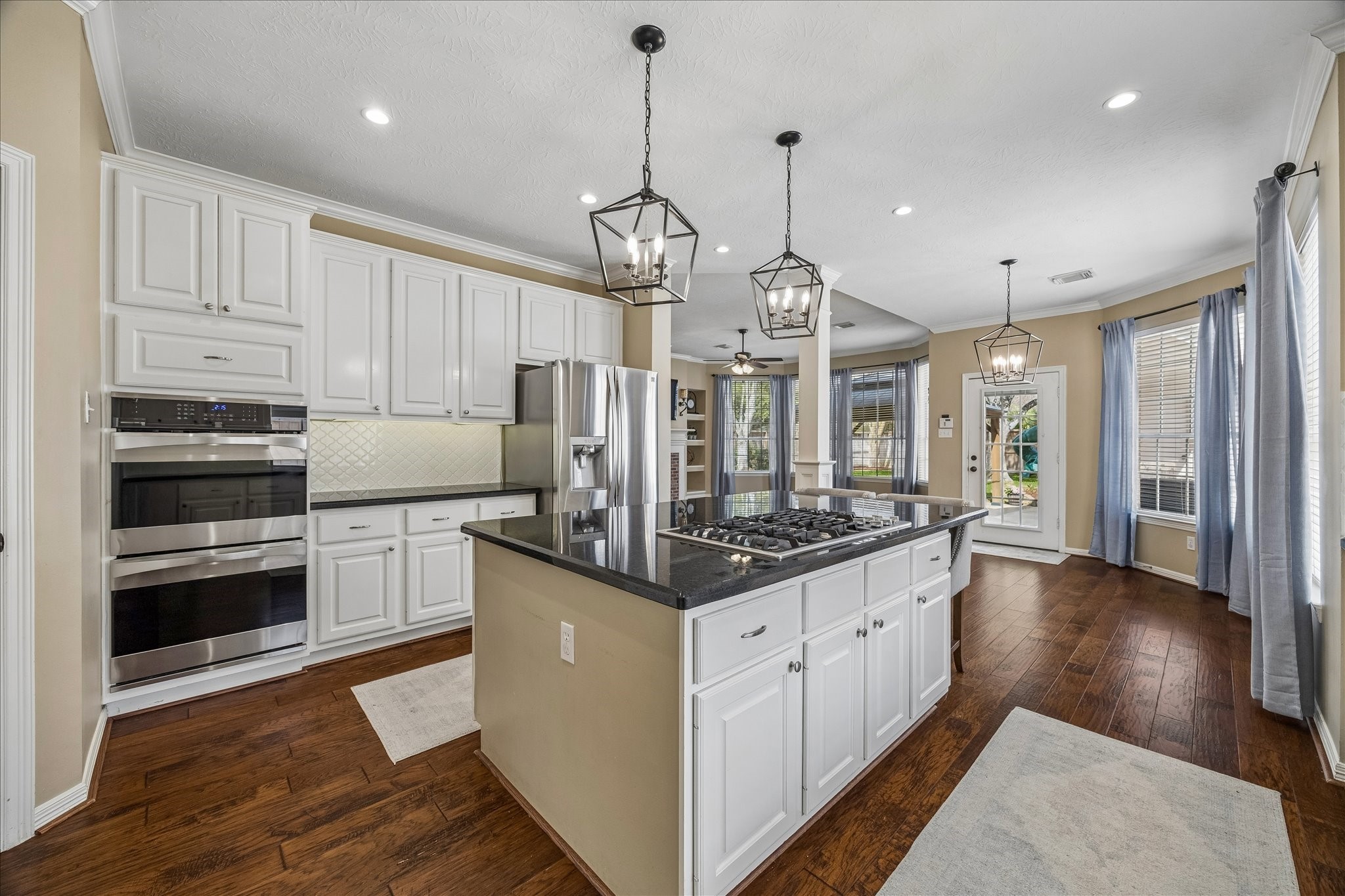 5310 Summerland Ridge Court Houston, TX 77041 - Photo 13 of 46 This spacious kitchen features elegant white cabinetry, a large island with a cooktop, modern stainless steel appliances, and stylish pendant lighting. The open layout flows into the dining area, enhanced by large windows and hardwood floors, creating a bright and inviting atmosphere.