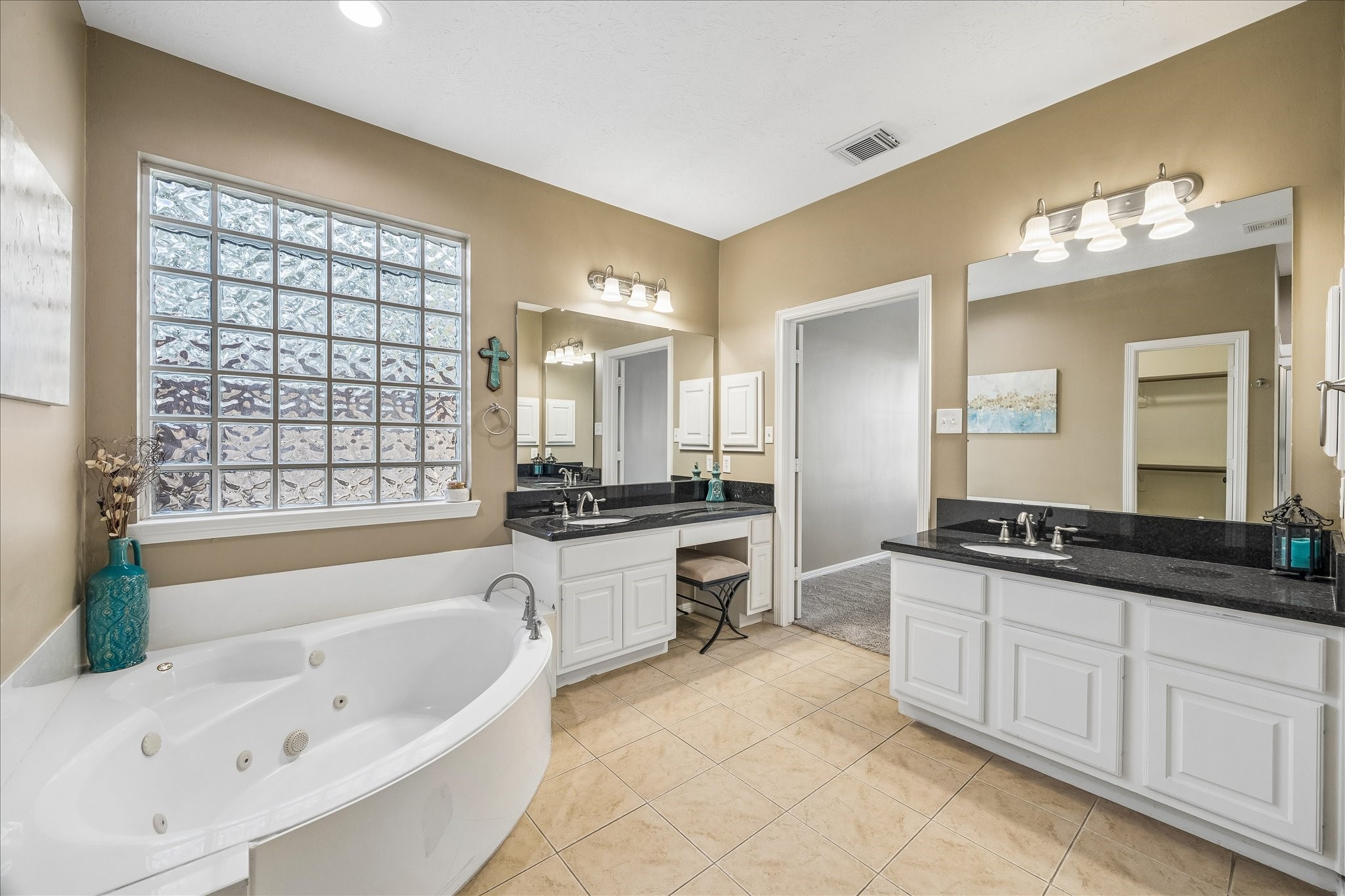 5310 Summerland Ridge Court Houston, TX 77041 - Photo 25 of 46 This spacious bathroom features a luxurious corner jacuzzi tub, dual sinks with granite countertops, and a vanity area. It has ample natural light from a large glass block window, elegant tile flooring, and modern light fixtures, creating a serene and functional space.