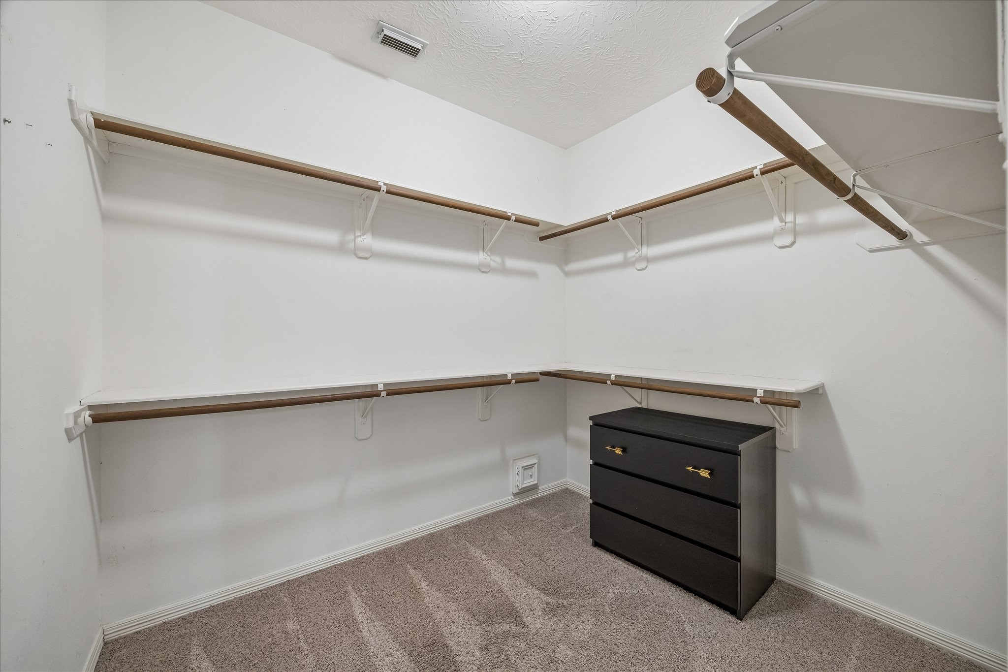 5310 Summerland Ridge Court Houston, TX 77041 - Photo 27 of 46 This photo shows a spacious walk-in closet with multiple wooden shelves and hanging rods for ample storage. The closet features neutral carpeting and includes a black dresser for additional organization.
