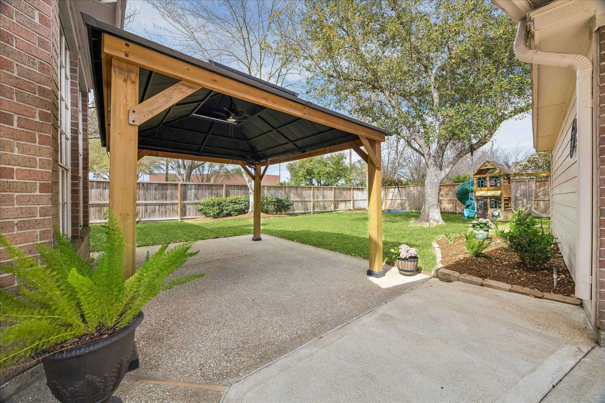 5310 Summerland Ridge Court Houston, TX 77041 - Photo 39 of 46 This backyard features a spacious covered patio with a wooden pergola, perfect for outdoor gatherings. The lawn is surrounded by a wooden fence for privacy, and includes a charming children's playset under a large tree. An inviting space for relaxation and family fun.