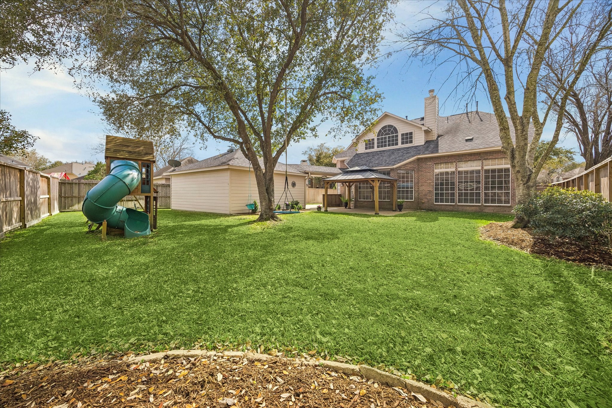 5310 Summerland Ridge Court Houston, TX 77041 - Photo 40 of 46 This spacious backyard features lush greenery, a playground set, and a charming gazebo, perfect for family activities and outdoor relaxation. The house has large windows, enhancing natural light.