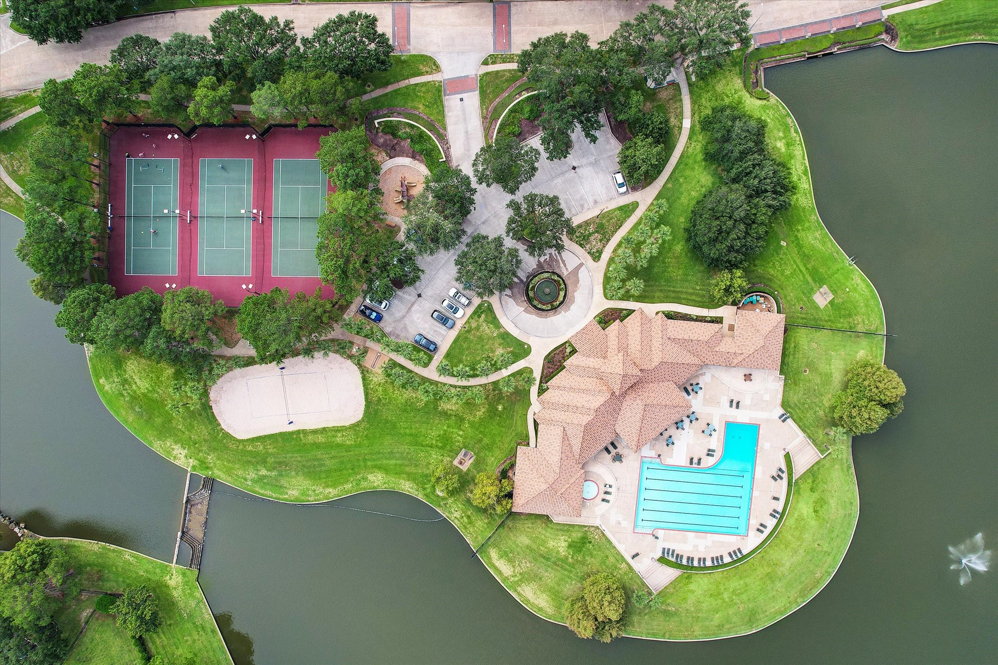 5310 Summerland Ridge Court Houston, TX 77041 - Photo 42 of 46 This aerial view showcases a scenic property featuring a large swimming pool, tennis courts, lush greenery, and a charming waterway. Ideal for active living and relaxation.