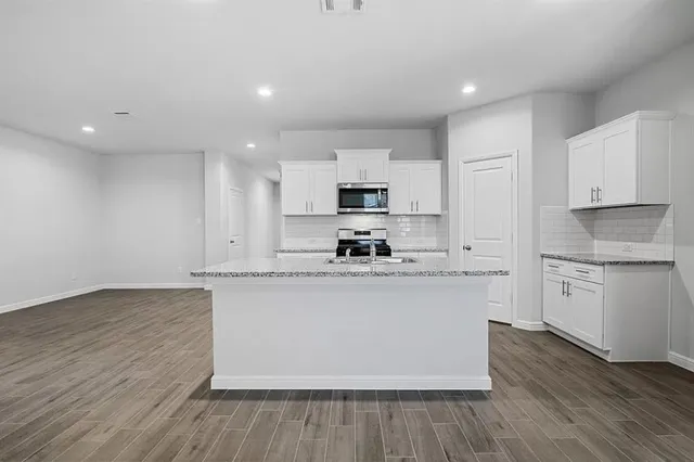 a kitchen with stainless steel appliances granite countertop a stove top oven a sink and white cabinets with wooden floor