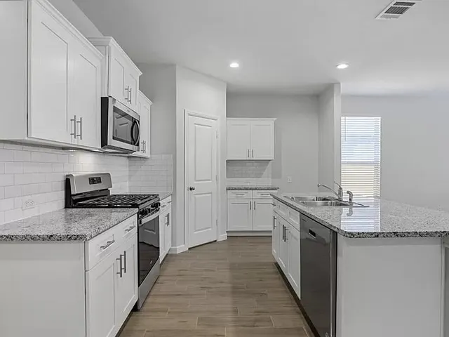 a kitchen with stainless steel appliances granite countertop a stove top oven a sink a refrigerator and white cabinets