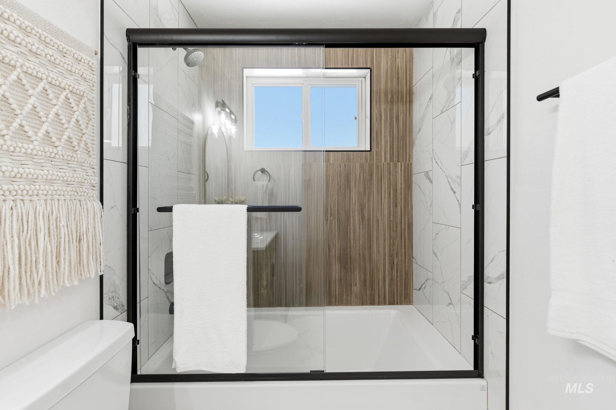 2224 Rachel Circle Boise, ID 83706 - Photo 33 of 50 Modern tub-shower combination featuring a black-framed glass enclosure, white subway tile with gray veining, wood-finish accent tile, and an integrated window