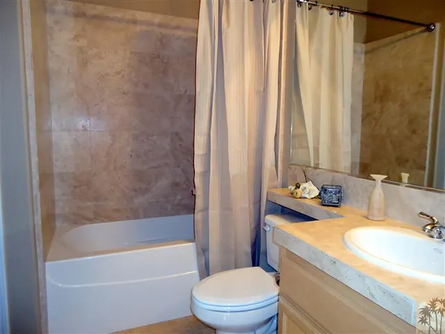 a bathroom with a granite countertop bathtub sink vanity mirror and toilet