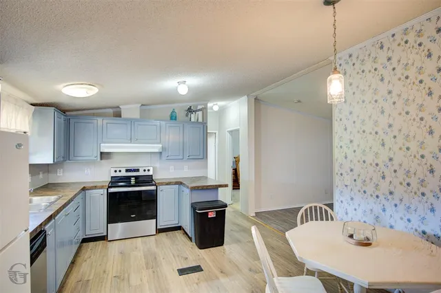 a kitchen with granite countertop a refrigerator a sink dishwasher a stove top oven a dining table and chairs with wooden floor