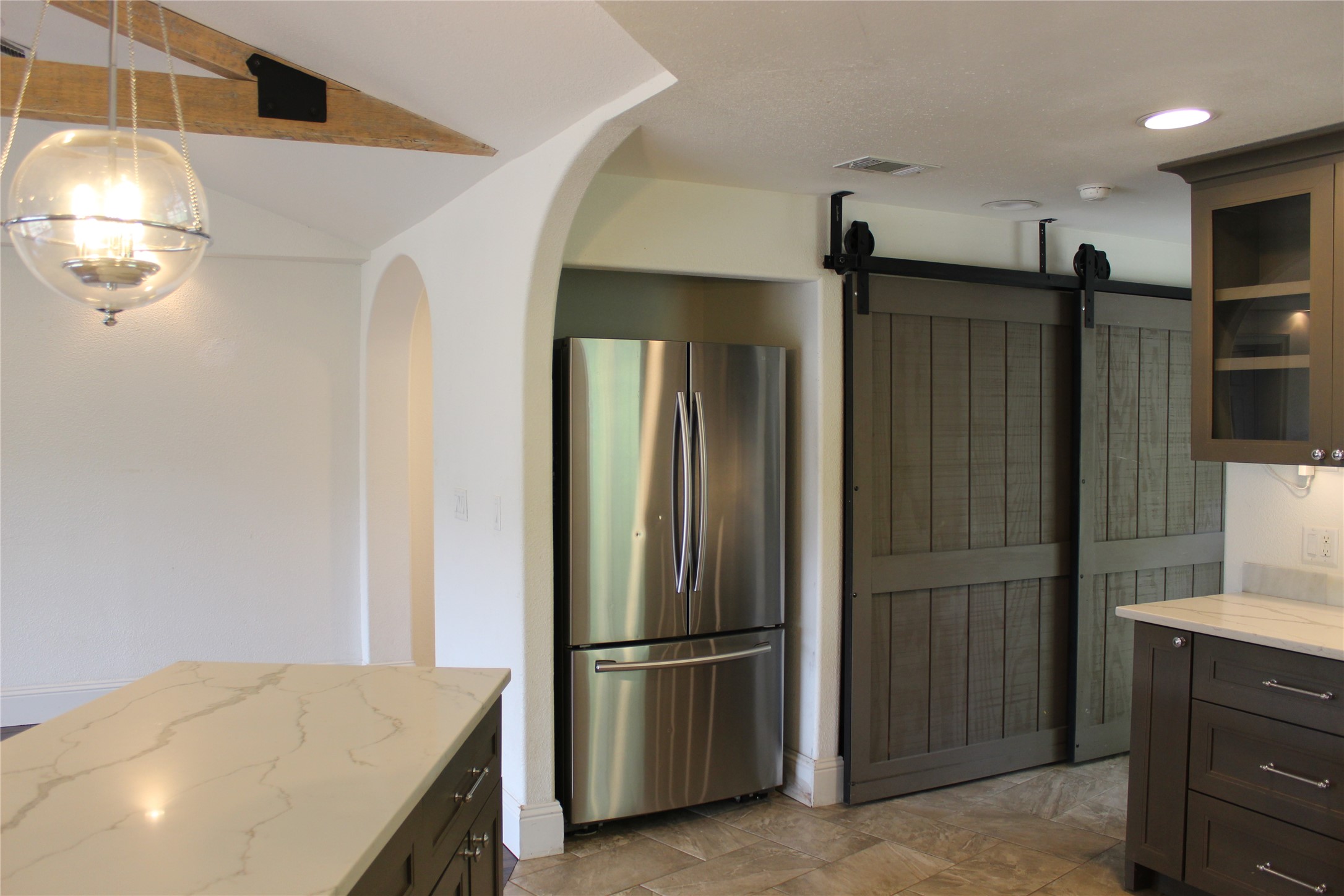 908 River Road Wimberley, TX 78676 - Photo 11 of 16 Kitchen featuring freestanding refrigerator, a barn door, glass insert cabinets, arched walkways, and light stone countertops