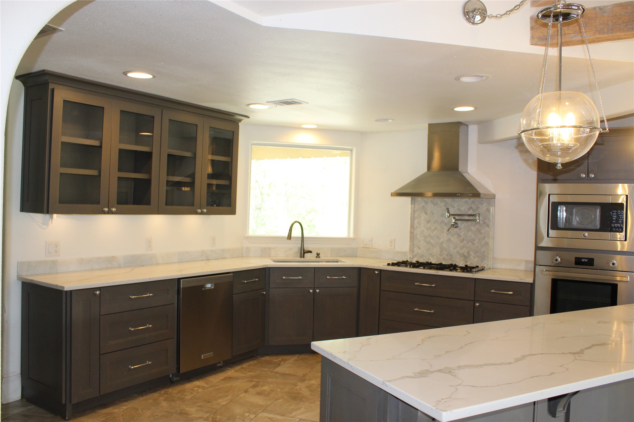 908 River Road Wimberley, TX 78676 - Photo 12 of 16 Kitchen featuring stainless steel appliances, glass insert cabinets, light stone counters, decorative backsplash, and arched walkways