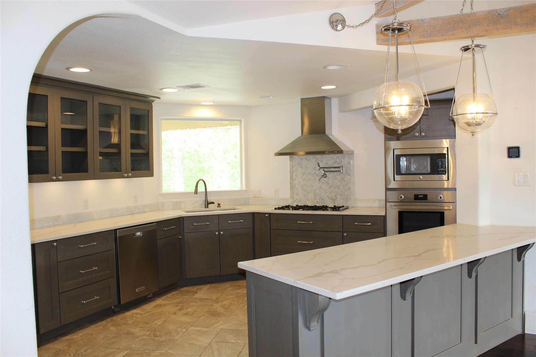 908 River Road Wimberley, TX 78676 - Photo 9 of 16 Kitchen with glass insert cabinets, a kitchen bar, stainless steel appliances, light stone countertops, and decorative backsplash