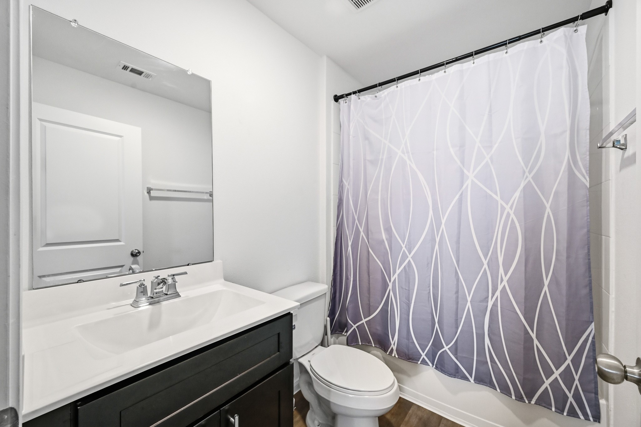 23427 Weir Box Road Hockley, TX 77447 - Photo 19 of 32 Features a modern dark vanity with a solid white countertop, sleek chrome fixtures, and a shower/tub combination with custom glass shelving for storage.