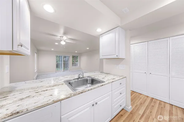 a kitchen with a sink dishwasher and white cabinets with wooden floor