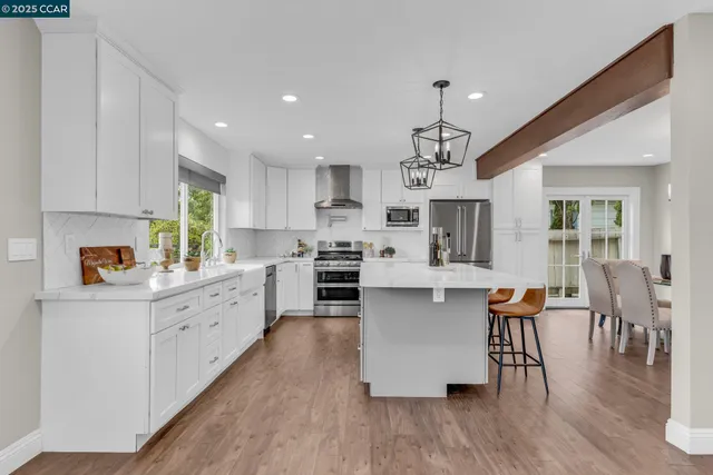 a kitchen with stainless steel appliances granite countertop a refrigerator a stove top oven a dining table and chairs with wooden floor