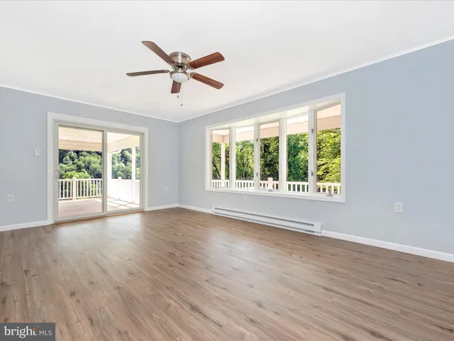an empty room with wooden floor ceiling fan and windows
