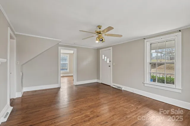 an empty room with wooden floor chandelier fan and windows