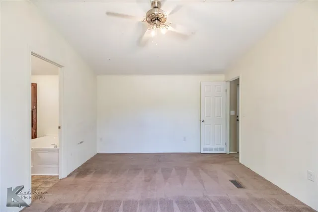 an empty room with chandelier fan and windows