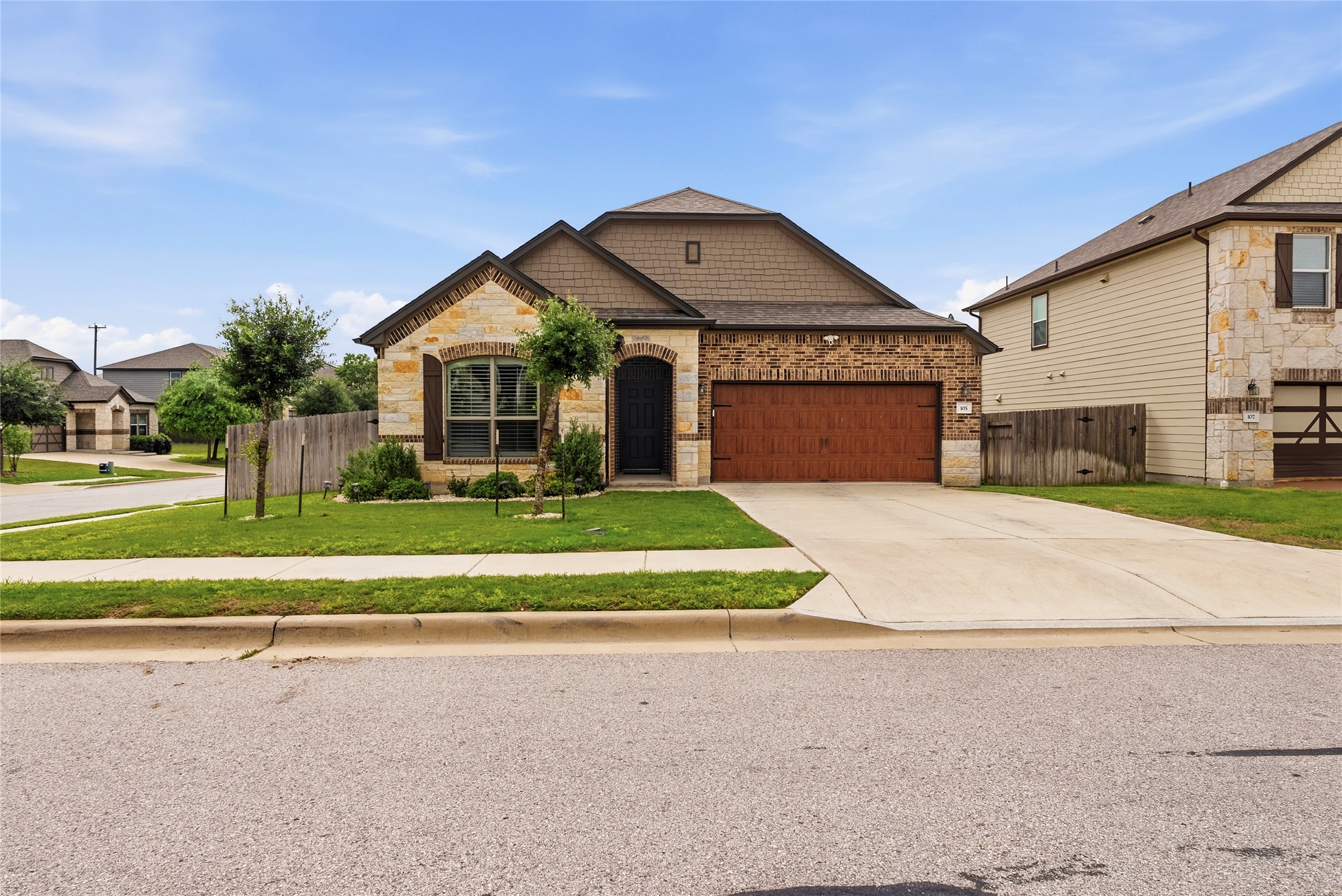 105 West Point Way Elgin, TX 78621 - Photo 1 of 27 Exterior featuring a combination of brick and stone siding, a wood-finish garage door, an arched entryway, mature landscaping, and an attached two-car garage