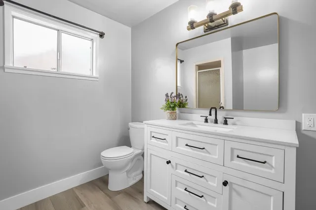 a bathroom with a toilet a sink a vanity a window and mirror