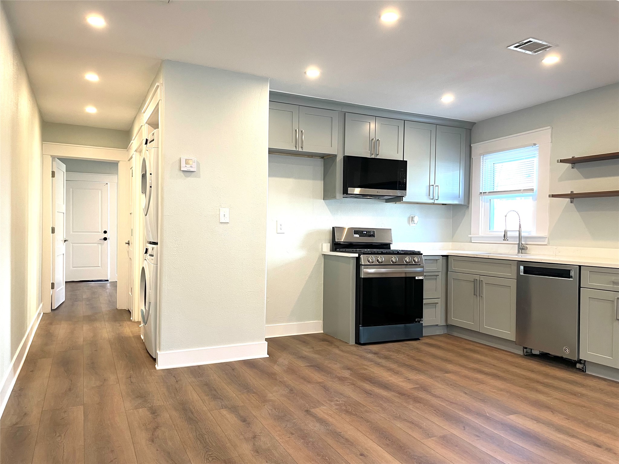 807 East Riverside Drive, Unit A Austin, TX 78704 - Photo 7 of 29 Kitchen with gray cabinets, stainless steel appliances, stacked washer / dryer, open shelves, and dark wood-type flooring