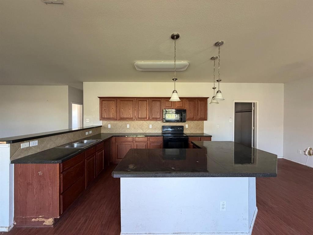10400 Wagon Rut Court Fort Worth, TX 76108 - Photo 16 of 26 Kitchen featuring black appliances, dark wood-style flooring, a center island, and decorative light fixtures