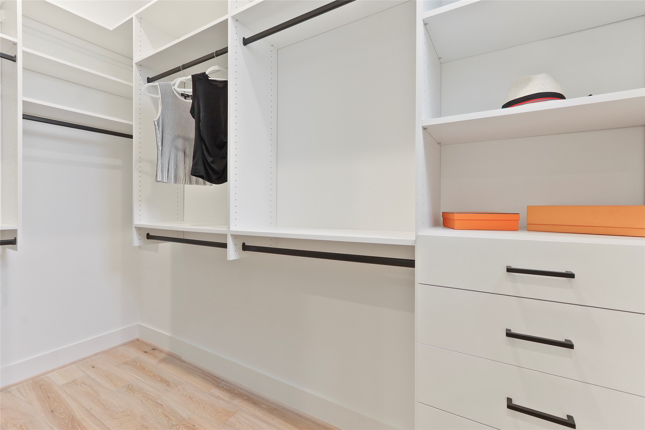 1141 West 17th Street, Unit A Houston, TX 77008 - Photo 13 of 18 Custom built walk in closet with light wood-style floors. The closet features custom built hanging space with black metal clothing rods, multiple drawers, folding shelves, built in laundry hampers, and multiple shoe shelves. Window lets in natural light.
