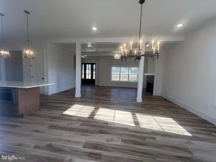 a view of an empty room with wooden floor and a kitchen